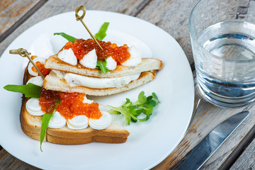 Classic breakfast, hot sandwich with red salmon caviar and mozzarella on a plate on a wooden table.