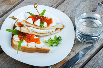 Classic breakfast, hot sandwich with red salmon caviar and mozzarella on a plate on a wooden table.