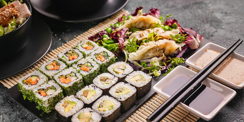 Banner asian food. Close up sushi rolls with vegetables and dumplings. Chinese cuisine on a gray concrete background