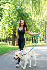 Cheerful pretty young woman walking and running with her dog in summer park. Active leisure, beautiful brunette girl at morning  jogging with puppy