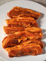 Korean style marinated pork belly slices, close up, on a white plate. Fresh meat preparation. Vertical image.