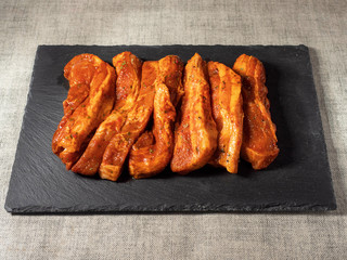 Korean style marinated pork belly slices, close up, on a black stone plate. Fresh meat preparation.