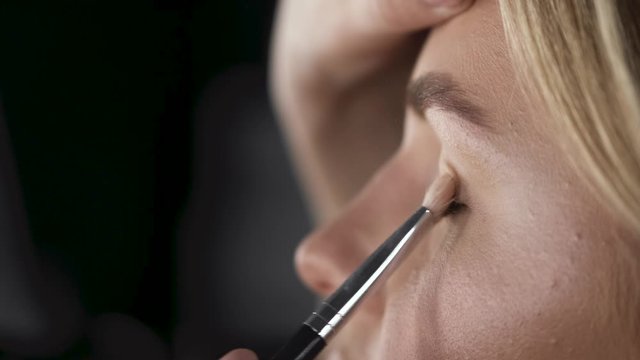 An artist is doing makeup for the client. The customer has a beautiful face. The girls are in a salon.