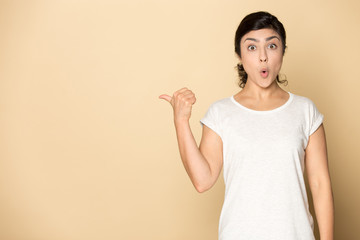 Astonished female indian ethnic customer pointing finger aside on copyspace.