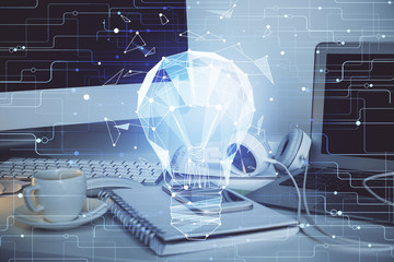 Computer on desktop in office with bulb icon hologram. Multi exposure. Concept of idea.