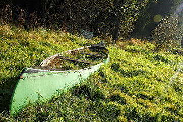 The old canoe is lying on the meadow close to the river and is abandoned, fully overgrown by grass and useless. 