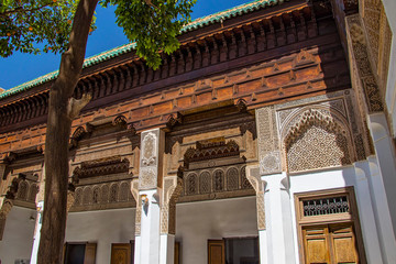 Obraz premium Detail of islamic building. It is an old architecture in the middle of the Moroccan city. There are white walls with wooden carved characters. There is summer time.