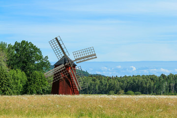 Fototapeta na wymiar The typical red Swedish windmill standing in the fields full of grain. The rural landscape of the Swedish countryside.
