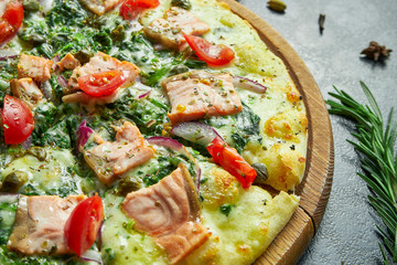Homemade baked pizza with salmon, white sauce, spinach, melted cheese, sweet onions and tomatoes on a black background in a composition with ingredients.