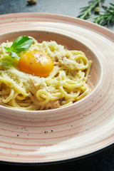Homemade and fresh carbonara pasta with yolk and parmesan. Italian appetizing spaghetti in a pink plate on a black background in a composition with ingredients