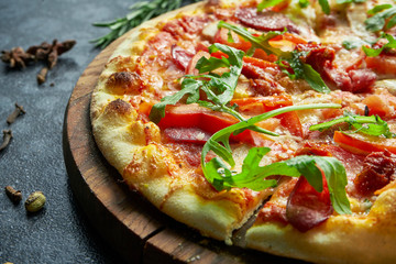 Homemade baked pizza with four kinds of meat, melted cheese, red sauce, tomatoes and ruccola on a black background in a composition with ingredients. Close up, selective focus