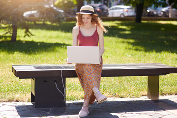 Outdoor shot of young woman working with her portable computer, charging her device on innovative...
