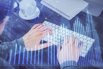 Double exposure of graph with man typing on computer in office on background. Concept of hard work.