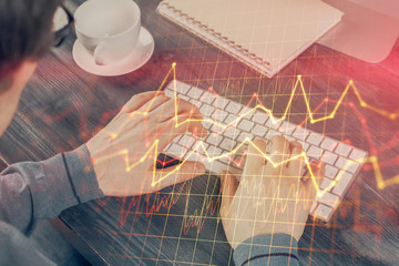 Double exposure of graph with man typing on computer in office on background. Concept of hard work.