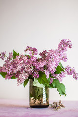 Spring purple lilac in a glass cup on a light background