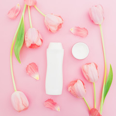 Shampoo with cream and tulips flowers on pink background. Flat lay