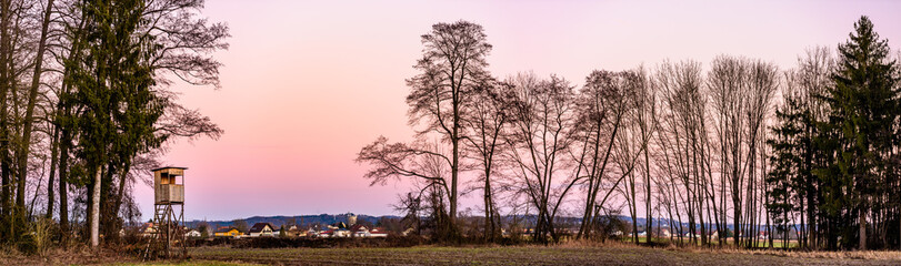 Fototapeta na wymiar Panorama landscape with hunting tower after sunset in rural scenery against pink sky. Deer stand near Zettling Graz in Austria. Hunting concept