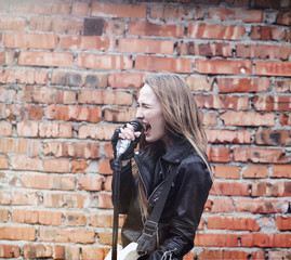 Fototapeta na wymiar Beautiful young girl rocker with electric guitar. A rock musician girl in a leather jacket with a guitar sings. A rock band soloist plays the guitar and screams into the microphone.
