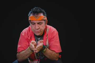 Shaman man, sorcerer, giving thanks duringPre-Hispanic ritual in Healing and cleaning with medicinal plants in Mexico, with black background
