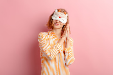 portrait of smiling girl with short hair, wearing pajamas and blindfold, want to sleep, she doesn't get enough sleep at morning, isolated pink background