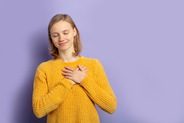 portrait of pleased young woman with closed eyes, wearing yellow casual blouse, stand smiling isolated over purple background