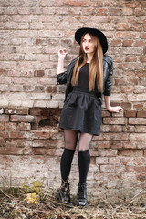 Young beautiful girl in a hat and with a dark make-up outside. Girl in the Gothic style on the street. A girl walks down the city street in a leather waistcoat with a phone.