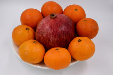 Orange tangerines are placed in a circle on one plate, and in the center is a large, red pomegranate. Fruit on a plate.