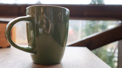 Green cup with tea or coffee on a wooden table on the balcony overlooking the street. Hot drink on the table on the veranda of the summer cafe. Soft focus.