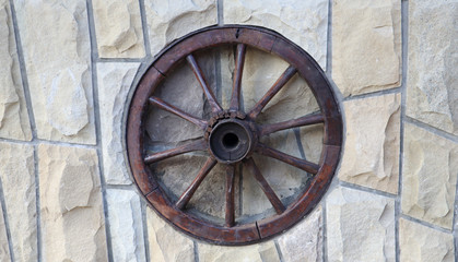 old wooden wheel from a cart on a stone wall of a rural house