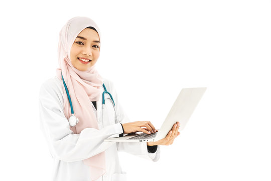 Portrait of beautiful young muslim woman doctor wearing doctor uniform and Hijab and Stethoscope using digital laptop computer, standing isolated on white background - Powered by Adobe