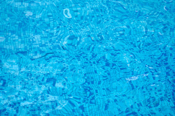 Background of water in blue swimming pool, water surface with a sun reflection