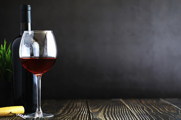 A glass of red dry wine on the table. Dark bottle and glass of wine.