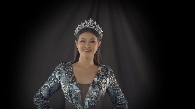 Miss beauty pageant contestant wears her crown in the spotlight, poses and smiles on the stage