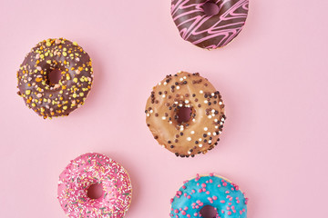Different types of a colorful donats decorated sprinkles and icing on pastel pink background