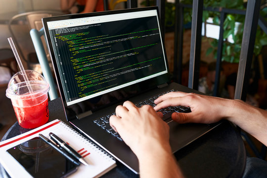 Developer programmer with laptop. Program code and script data on screen. Young freelancer in glasses working on project in cafe. Back view over the shoulder shot