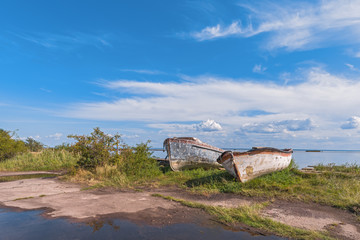 Two old boats lie on the shore in the wet grass after rain in summer day.