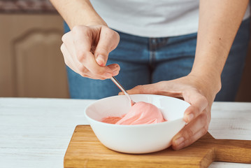 Woman whisking red cream for decorating cookies in a bowl on kitchen, closeup