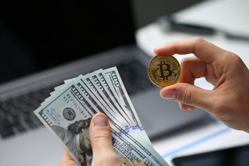 Male hand holds bitcoin and dollar growth on background of laptop keyboard