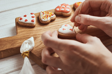 Decorating gingerbread cookies with icing. Woman hand decorate cookies in shape of heart, closeup
