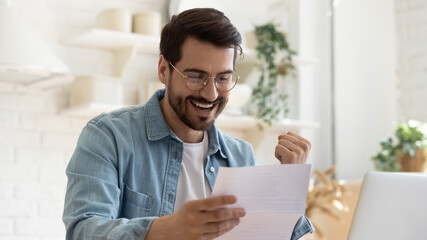 Happy young man reading paper letter with good news.