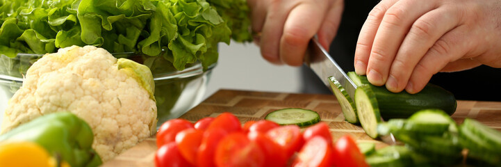 Cook holds knife in hand and cuts on cutting board green cucumber for salad or fresh vegetable soup...