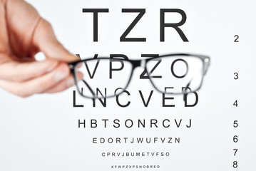 Glasses on a white background. Background with letters for vision test. The glasses are blurred. Sharpness on the text.