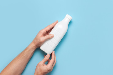 White plastic bottle containers for dairy products in male hands on blue background top view flat lay. Plastic Kefir Yogurt Milk Bottle. Packaging template mockup. Layout for your design