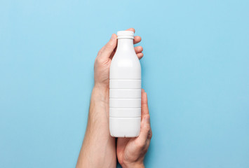 White plastic bottle containers for dairy products in male hands on blue background top view flat...