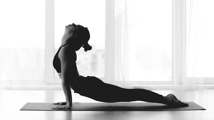 Girl making cobra yoga pose on mat, black and white photo