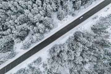 Aerial view of winter road with a car and snow covered forest in Finland
