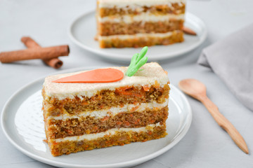 National Carrot Cake Day.  Carrot cake with cream cheese frosting decorated with chocolate carrots on a light wooden background. Close-up, top view