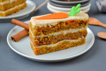 National Carrot Cake Day.  Carrot cake with cream cheese frosting decorated with chocolate carrots on a gray wooden background. Close-up, top view