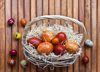Wicker basket with colored Easter eggs on a wooden background. View from above. Easter still life. Place for text at the top