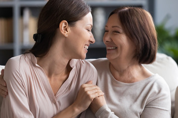 Happy adult mother and daughter share secrets at home